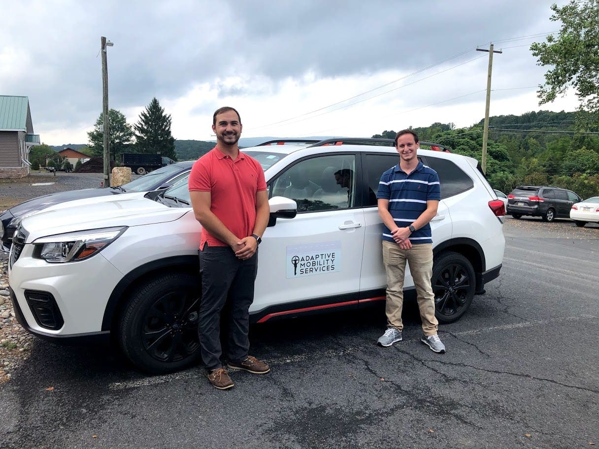 Two driver rehab specialists standing next to a white Adaptive Mobility SUV.