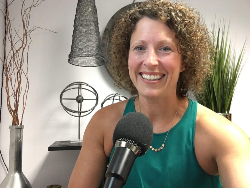 Susie Touchinsky smiling. A podcasting microphone is in front of her.