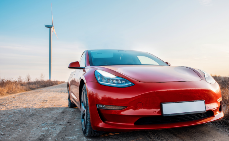 A red Tesla car on a dirt road. A windmill is in the background.